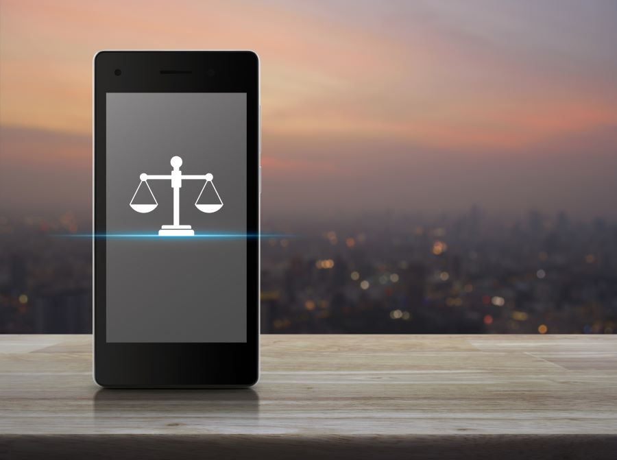 a smartphone displaying a glyph of the scales of justice with a cityscape at sunset in the background