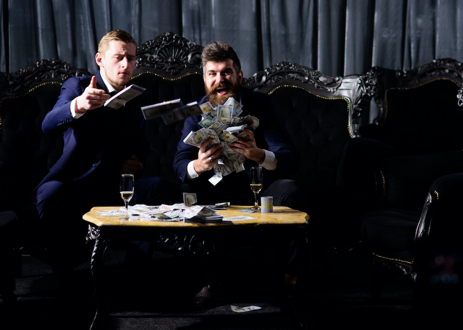 Two men in suits celebrate with cash in a dark room