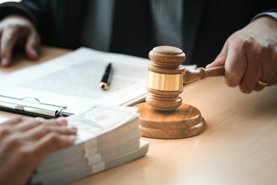 A person in a suit bangs a gavel while another person slides a stack of money toward them