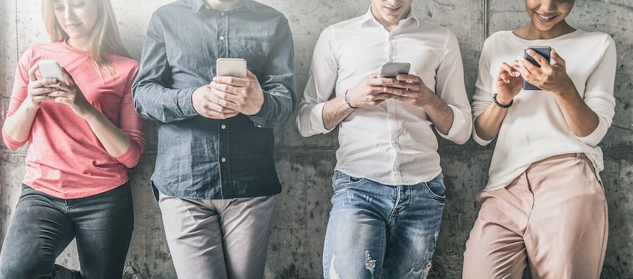 people leaning against a wall, looking at smart phones