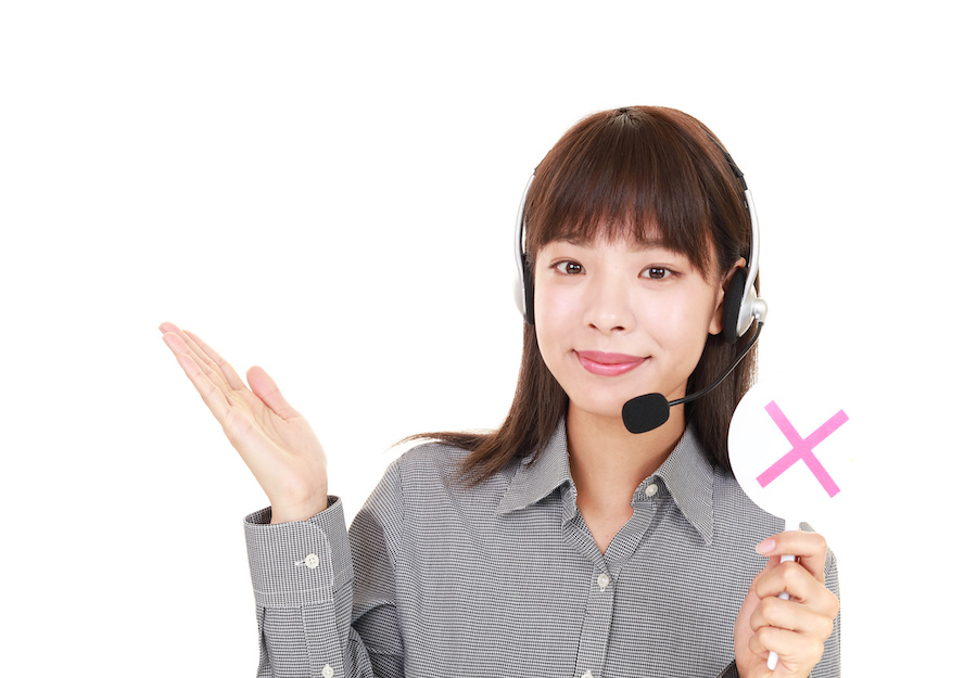 A woman with a headset telephone raises her right palm and holds a sign with a red X in her left hand