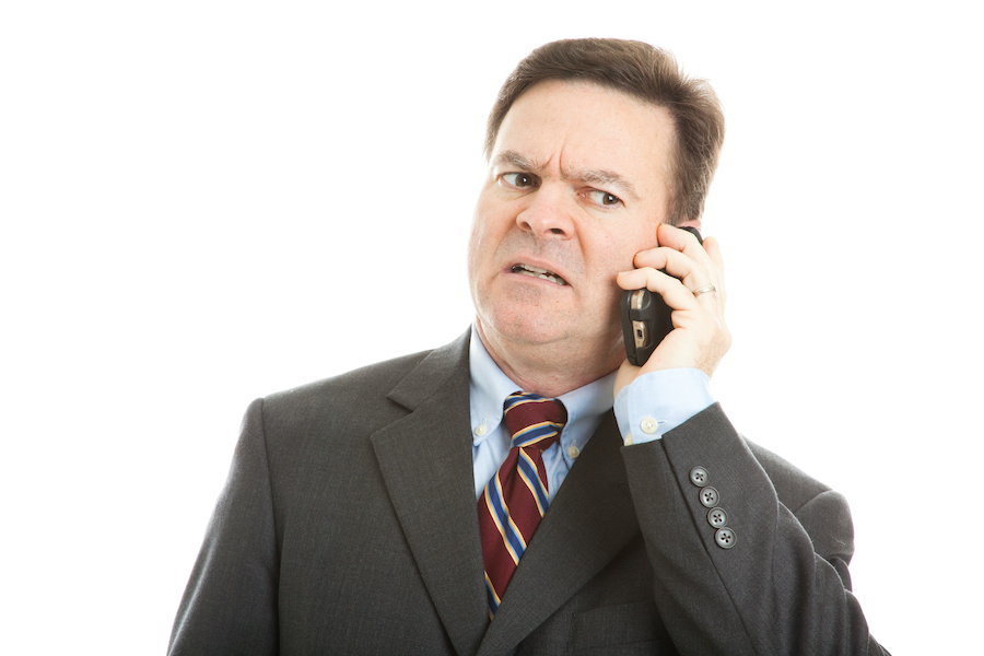 A man in a suit answers his smartphone and looks dismayed