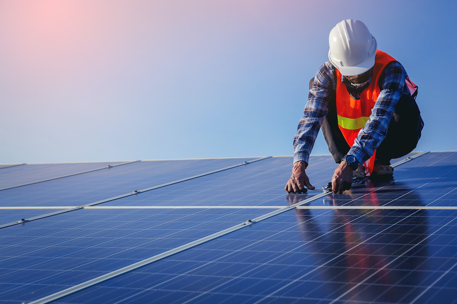 A man in an orange vest and hard hat works to install solar panels.