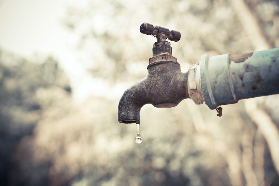 a drop of water falls from an outdoor faucet