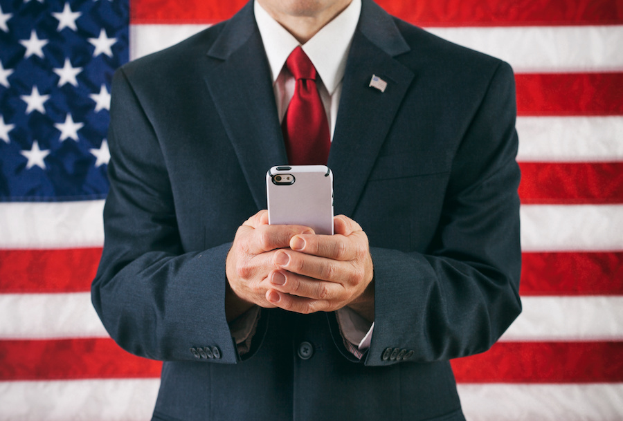 a man in a business suit sends a text message while standing in front of the American flag