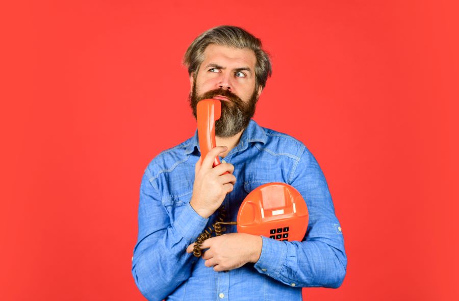 A bearded man cradles an orange phone with a plaintive look on his face