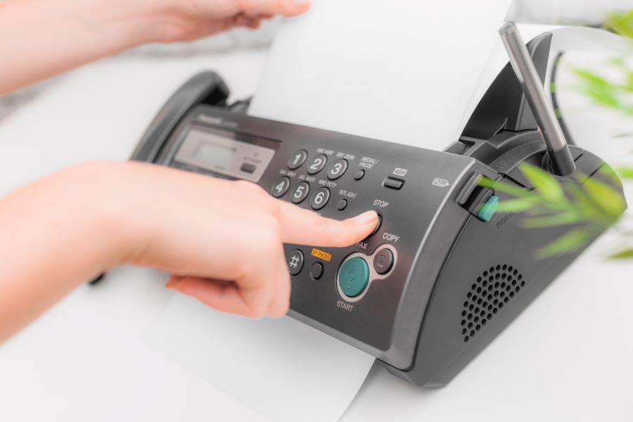 A finger presses the stop button on a fax machine