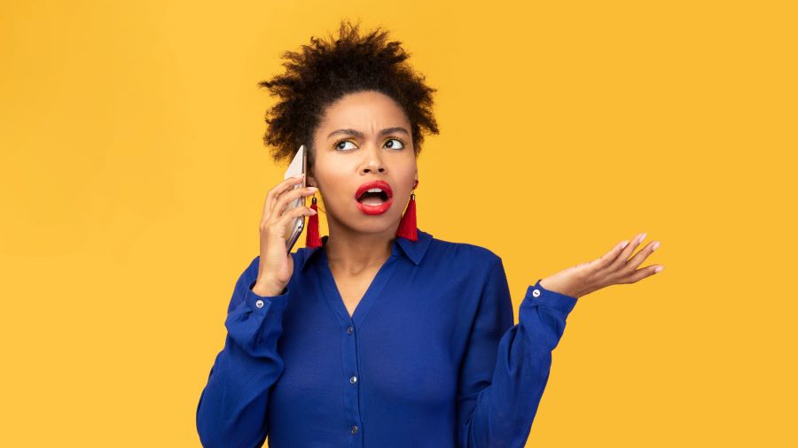 A woman in front of an orange background answers her phone and is annoyed