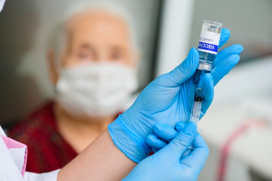 a nurse holds a syringe and a glass jar labeled covid-19 vaccine and prepares to vaccinate an elderly woman for the prevention of coronavirus infection