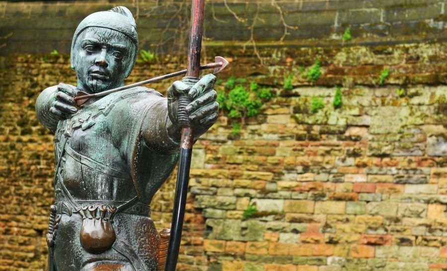 A brass statue of a medieval archer resembling Robin Hood is in front of a dilapidated brick wall