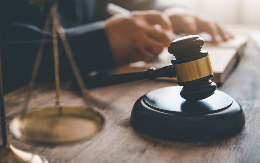 A scale of justice and gavel in the foreground, somebody signing a contract in the background