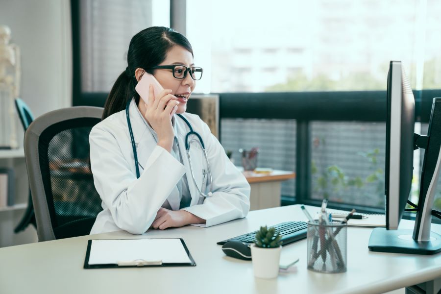 A doctor sits at her desk and has a conversation on a cell phone