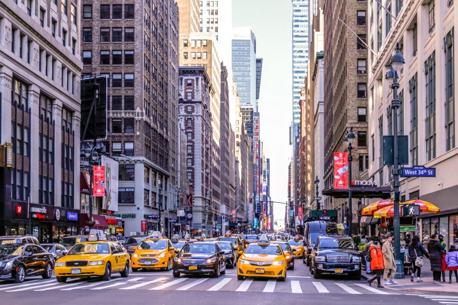 Looking down a Manhattan avenue with cars, taxis, pedestrians, hot dog carts, tall buildings, Macy's