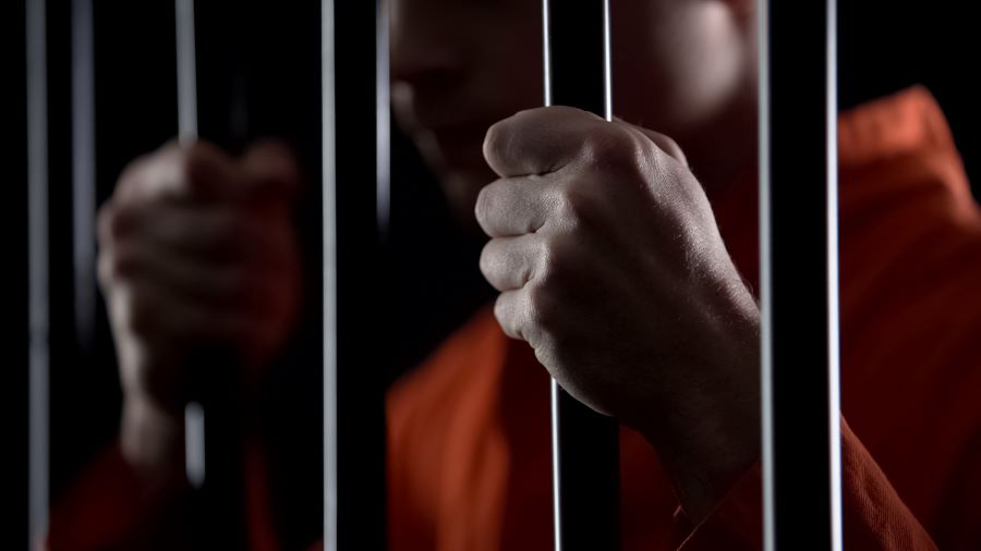 A prisoner holds the bars of a jail cell