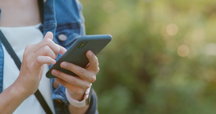 A woman in a denim shirt is using a smartphone while out in nature