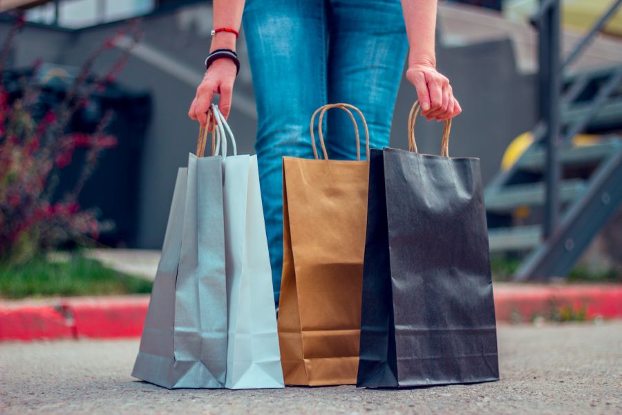 Woman dressed in blue jeans prepare to grab shopping bags placed in front of her.