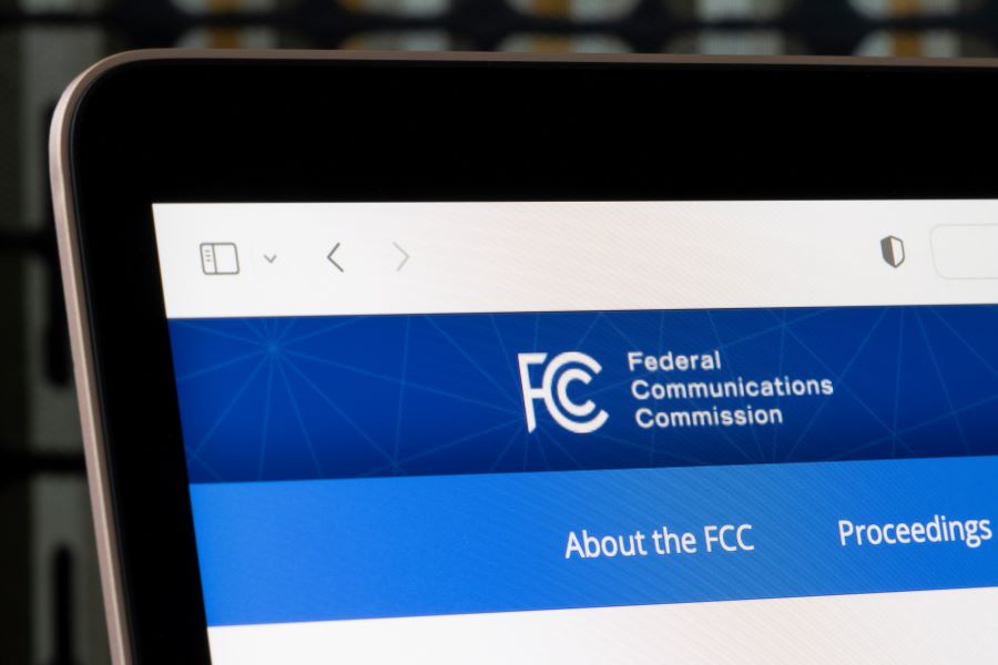 The top left corner of a laptop screen displays part of the header for the FCC's website